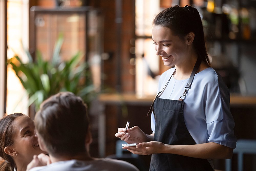 Illustrerende afbeelding van een bedieningsmedewerker die een bestelling opneemt bij 2 gasten in een restaurant.